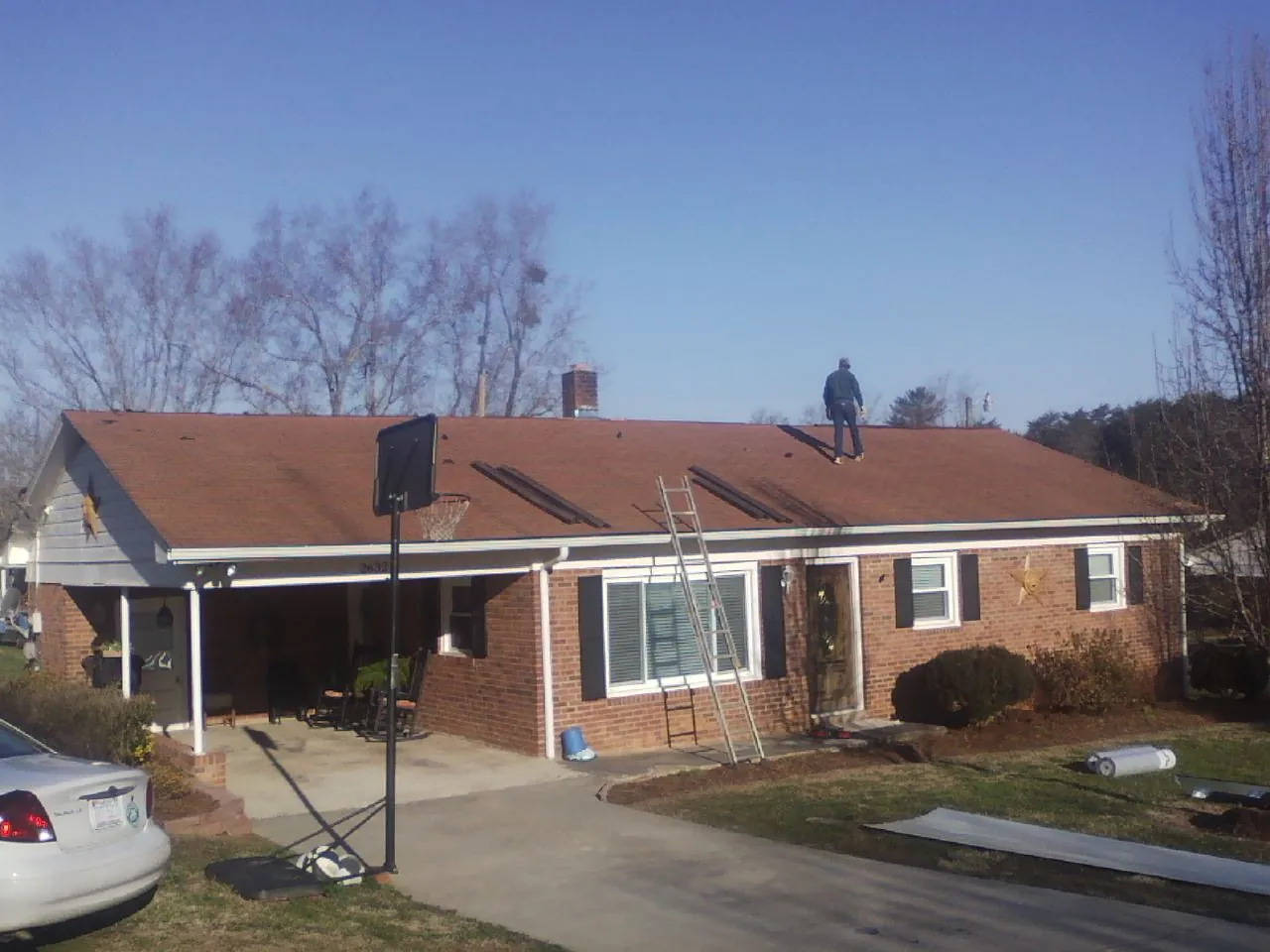 Roofer stripping a shingle roof on a brick ranch before metal panels in Bergenfield
