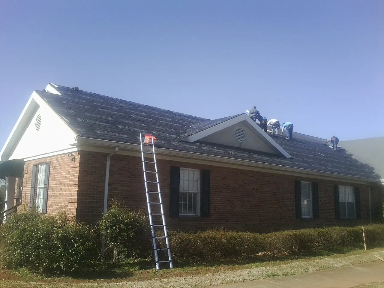 Crew tearing shingles off a brick ranch roof with a ladder set — Emergency Roof Repair work by our crew in Bergenfield
