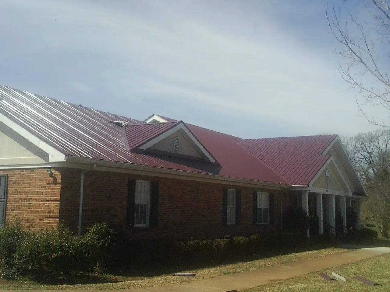 Red metal roof with gabled entries on a long brick building, from a Hail Damage Roof Repair job in Bergenfield