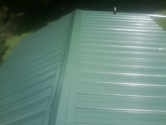 New green metal panels meeting at the ridge of a roof — Flat Roof Repair work by our crew in Bergenfield