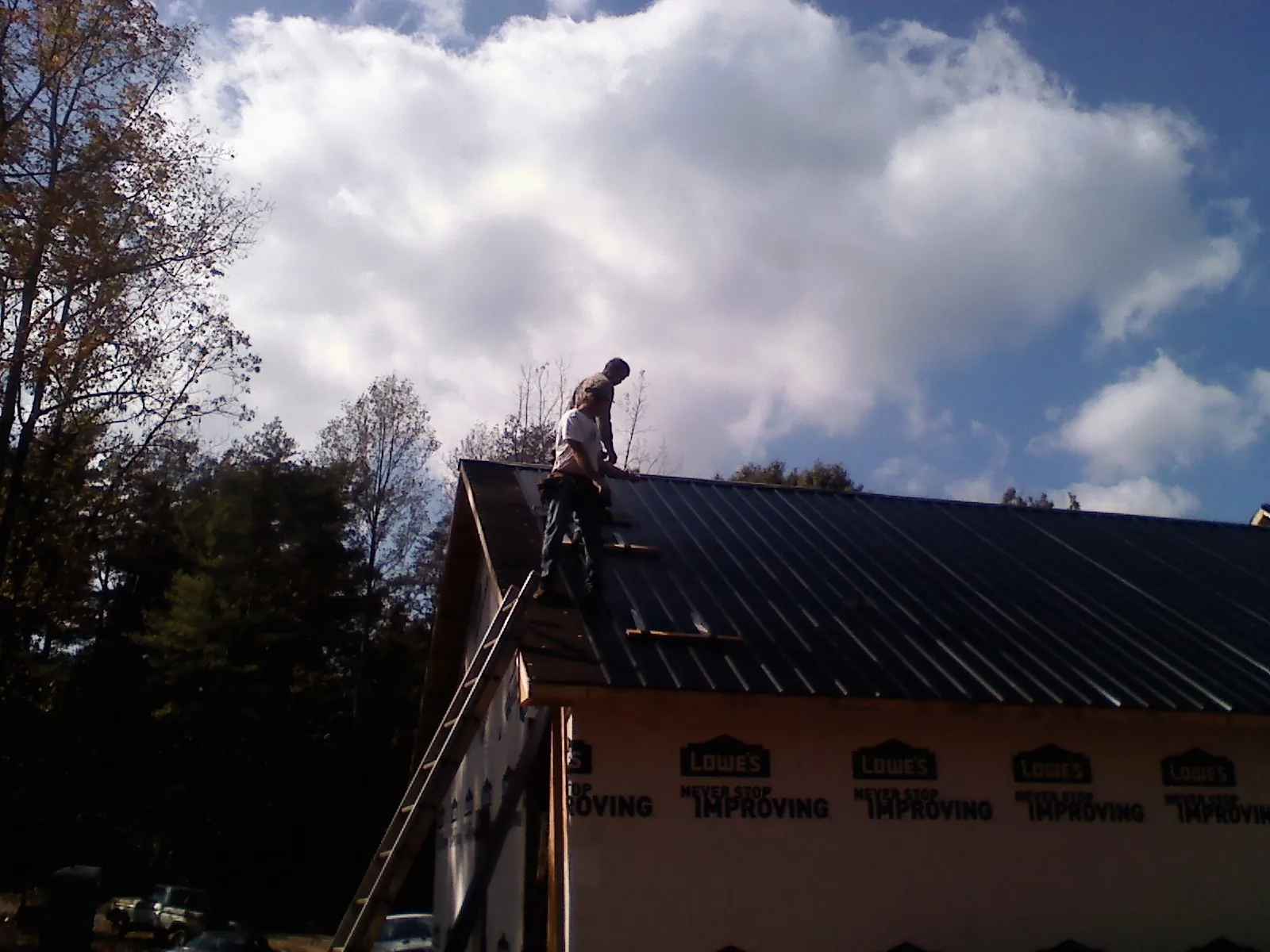 Roofer fastening dark metal panels high against a cloudy sky, from a Roof Inspection job in Bergenfield