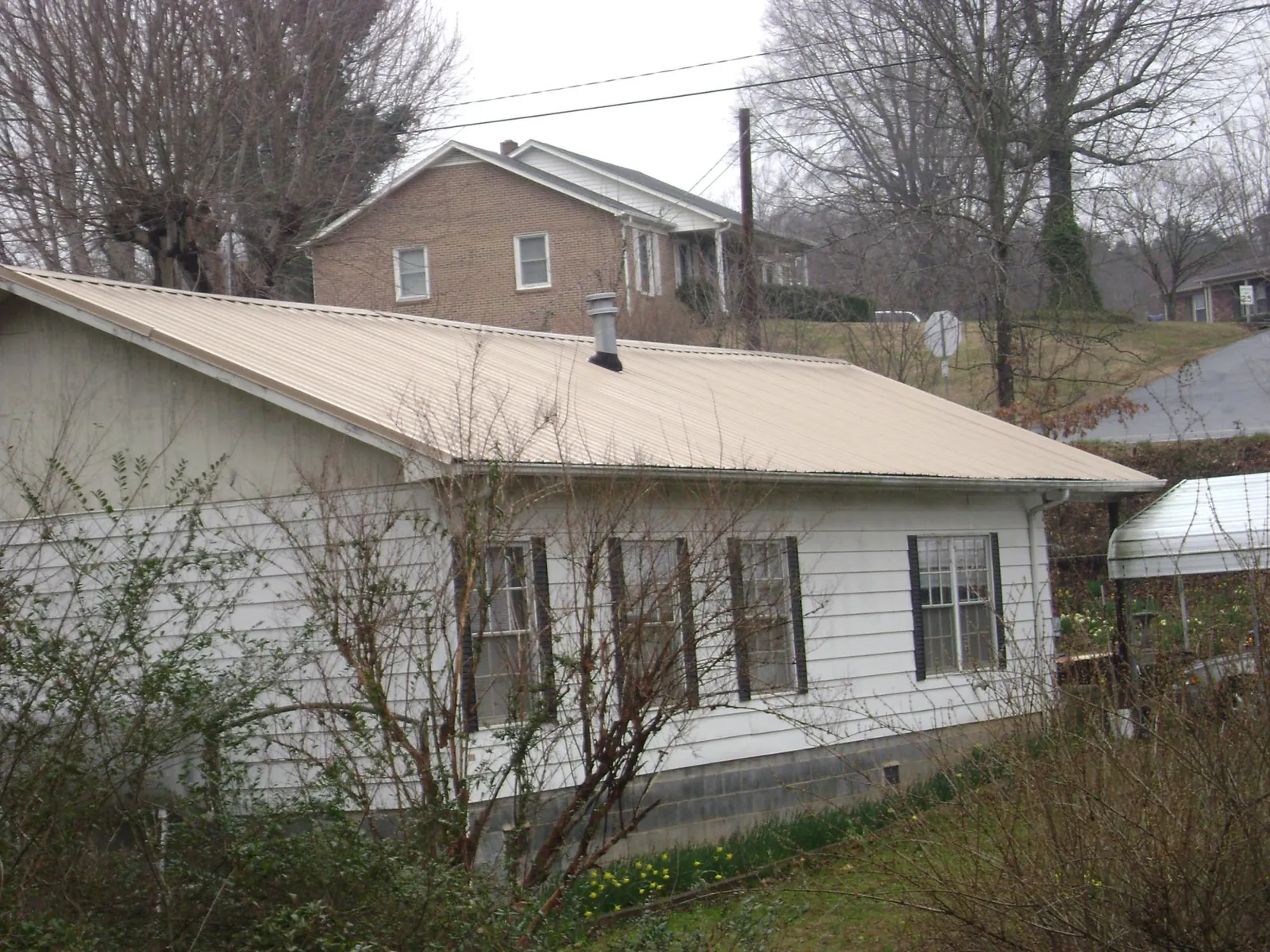 Tan metal roof on a white sided house set into a hillside — Commercial Roofing by Roofing Brothers in Bergenfield